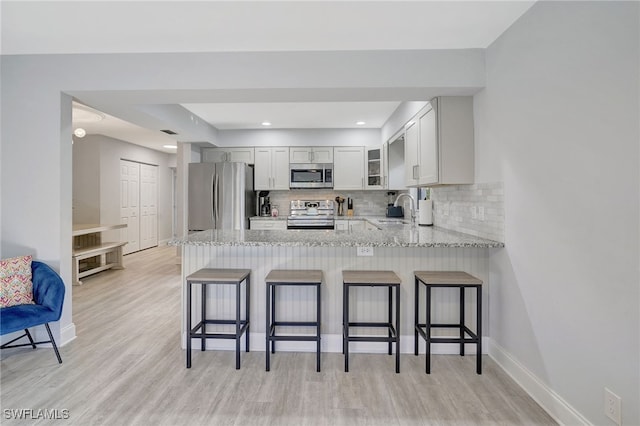 kitchen with light stone counters, stainless steel appliances, backsplash, a sink, and a peninsula