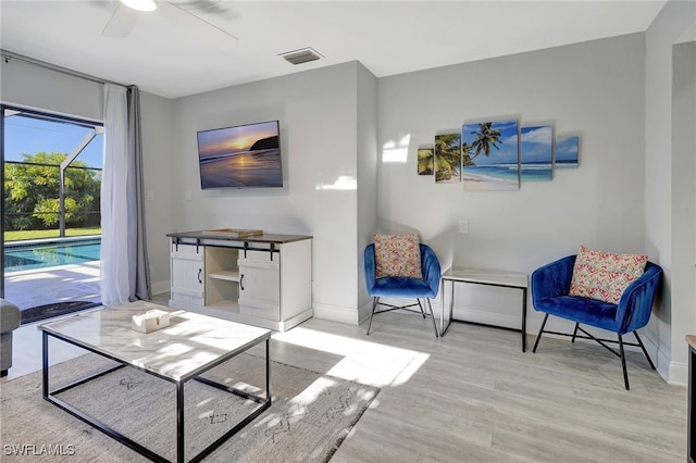 sitting room with a ceiling fan, visible vents, baseboards, and wood finished floors