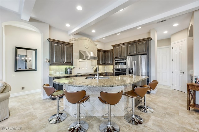 kitchen with decorative backsplash, appliances with stainless steel finishes, sink, beam ceiling, and wall chimney exhaust hood