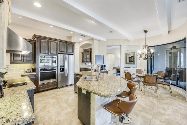 kitchen with appliances with stainless steel finishes, beamed ceiling, light tile patterned floors, sink, and wall chimney range hood