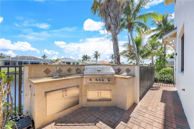 view of patio with exterior kitchen, a grill, sink, and a water view