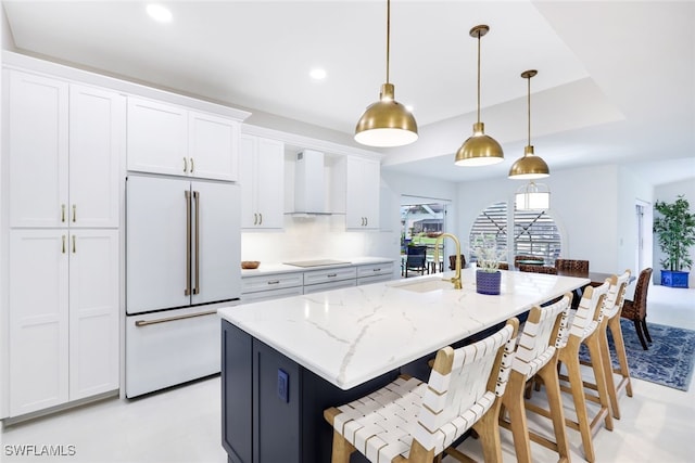 kitchen featuring pendant lighting, wall chimney exhaust hood, white cabinetry, light stone counters, and high end white refrigerator