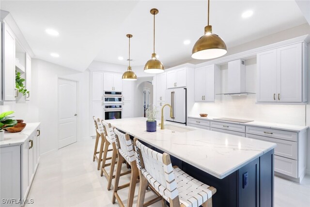 kitchen with wall chimney range hood, pendant lighting, tasteful backsplash, high end white fridge, and a center island with sink