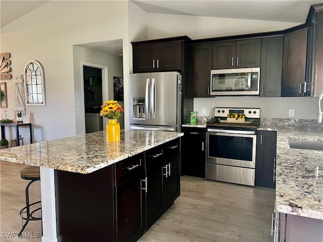 kitchen with vaulted ceiling, light stone counters, stainless steel appliances, light hardwood / wood-style floors, and a kitchen island