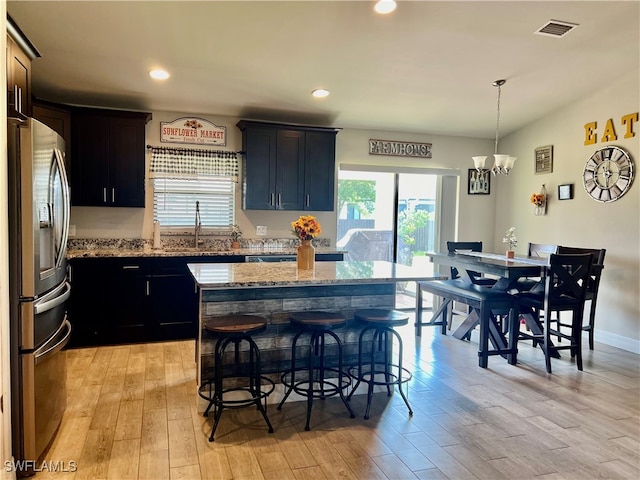 kitchen with a center island, light wood-type flooring, decorative light fixtures, light stone countertops, and stainless steel refrigerator with ice dispenser