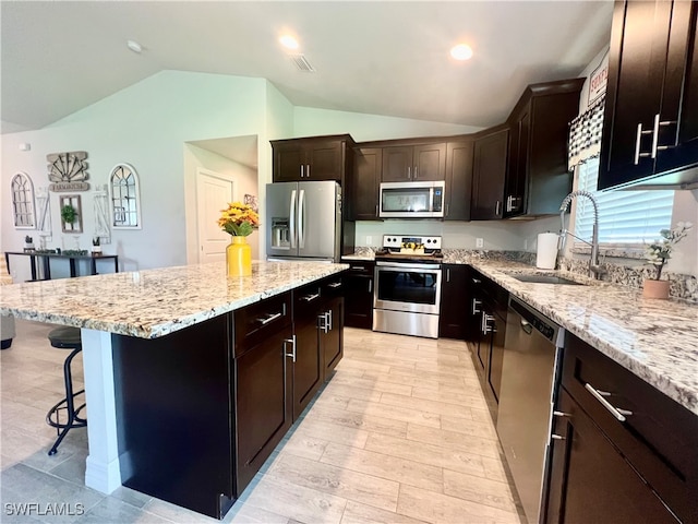 kitchen with light wood-type flooring, vaulted ceiling, a center island, sink, and appliances with stainless steel finishes