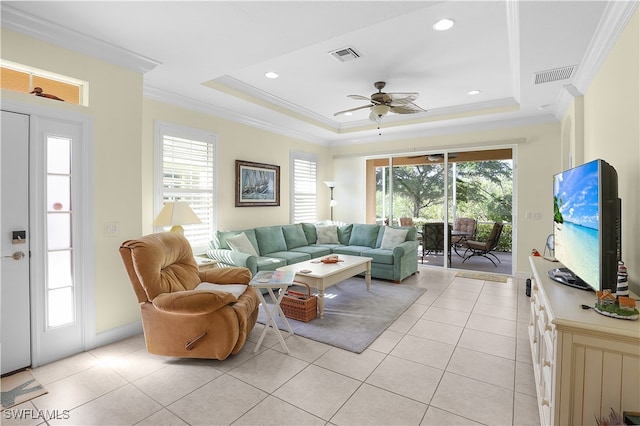 tiled living room with ceiling fan, a tray ceiling, and ornamental molding