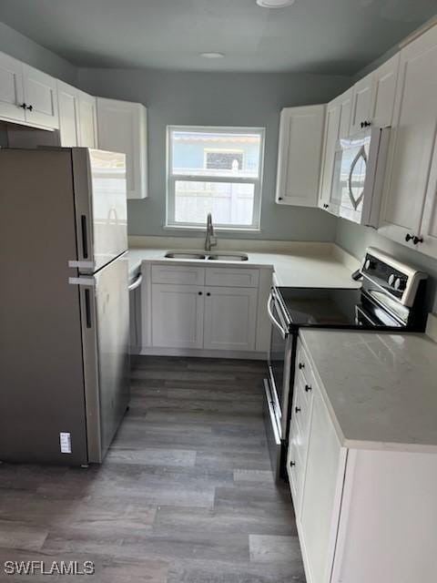 kitchen with wood-type flooring, white cabinetry, sink, and appliances with stainless steel finishes