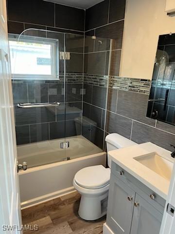 full bathroom with vanity, tiled shower / bath, toilet, tile walls, and wood-type flooring