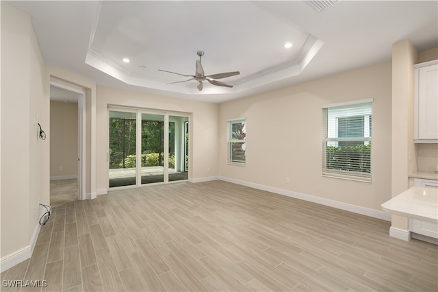 empty room with ceiling fan, a tray ceiling, and plenty of natural light