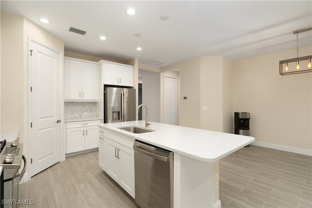 kitchen with hanging light fixtures, appliances with stainless steel finishes, a center island with sink, sink, and tasteful backsplash