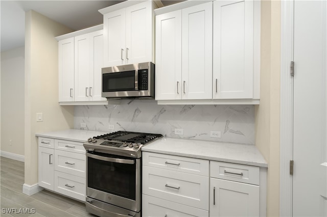 kitchen with white cabinetry, appliances with stainless steel finishes, light stone countertops, backsplash, and light wood-type flooring