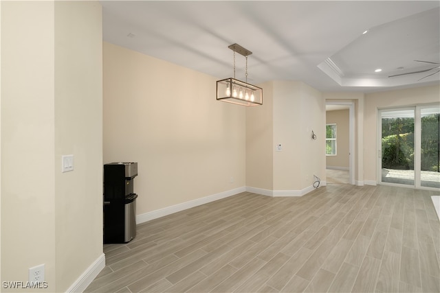 spare room featuring a tray ceiling, a chandelier, and light hardwood / wood-style floors