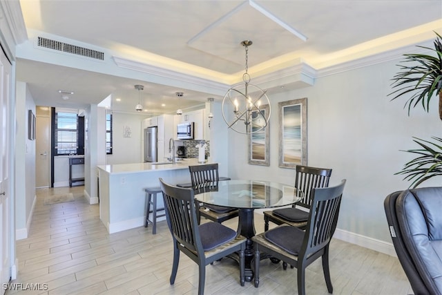 dining area with sink, an inviting chandelier, and a tray ceiling