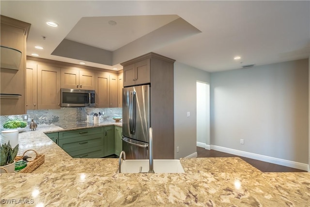 kitchen with a tray ceiling, backsplash, recessed lighting, appliances with stainless steel finishes, and baseboards