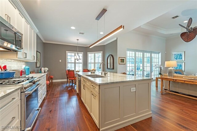 kitchen featuring appliances with stainless steel finishes, light stone counters, sink, dark wood-type flooring, and a kitchen island with sink