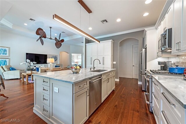 kitchen with appliances with stainless steel finishes, light stone counters, a center island with sink, and white cabinetry