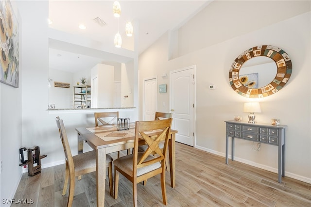 dining room with high vaulted ceiling and light hardwood / wood-style flooring