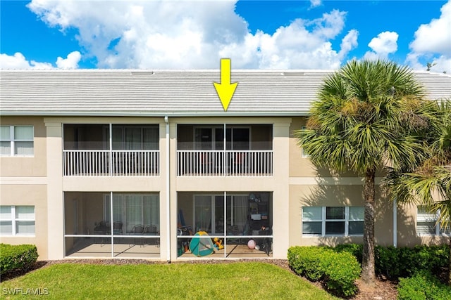 rear view of property featuring a balcony, a sunroom, and a yard