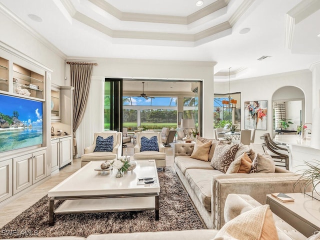 living area featuring light wood-style floors, visible vents, ornamental molding, and a tray ceiling