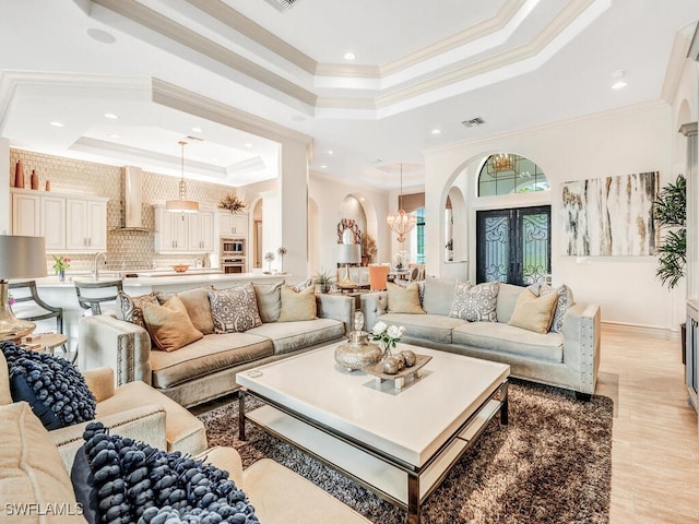 living area with a tray ceiling, arched walkways, a notable chandelier, visible vents, and ornamental molding