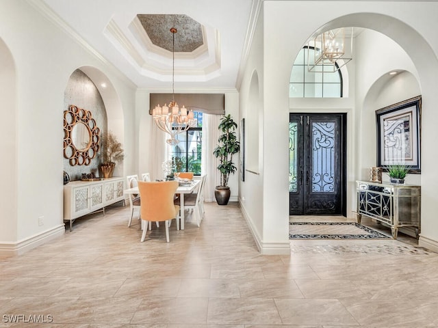 foyer entrance with crown molding, a tray ceiling, baseboards, and an inviting chandelier