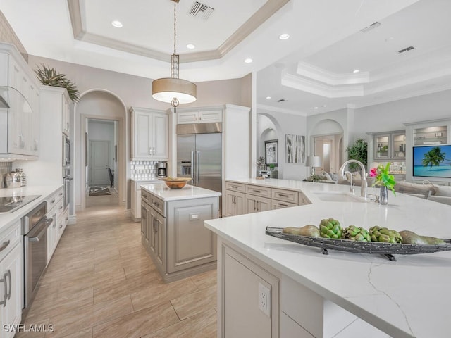 kitchen featuring visible vents, a raised ceiling, open floor plan, built in appliances, and a sink