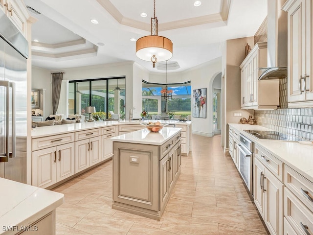 kitchen with cream cabinets, stainless steel appliances, a kitchen island, wall chimney exhaust hood, and a tray ceiling