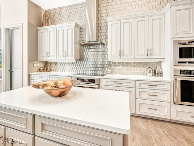 kitchen featuring light stone counters, decorative backsplash, appliances with stainless steel finishes, a kitchen island, and wall chimney exhaust hood