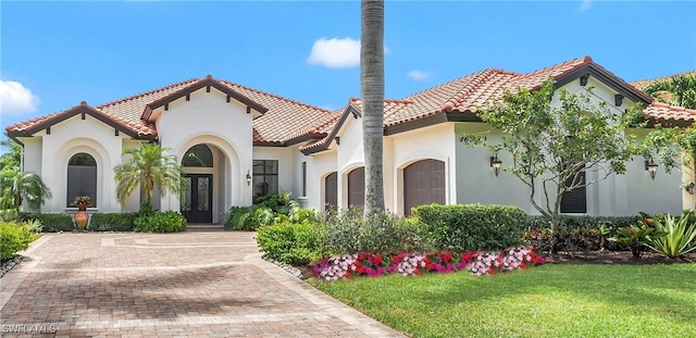 mediterranean / spanish-style house with an attached garage, a tiled roof, a front lawn, and stucco siding