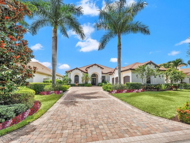 mediterranean / spanish house featuring an attached garage, a tile roof, decorative driveway, stucco siding, and a front yard