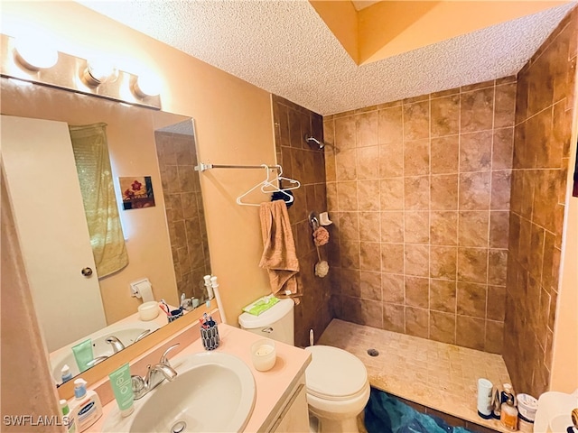 bathroom featuring a tile shower, a textured ceiling, vanity, and toilet