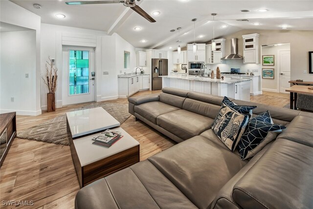 living area featuring lofted ceiling with beams, light wood finished floors, baseboards, and a ceiling fan