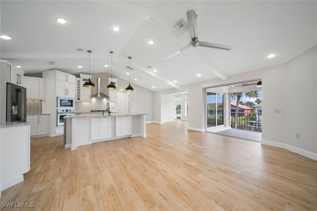 kitchen featuring oven, refrigerator with ice dispenser, open floor plan, wall chimney range hood, and built in microwave