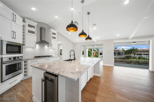 kitchen with wine cooler, stainless steel appliances, white cabinetry, sink, and wall chimney range hood