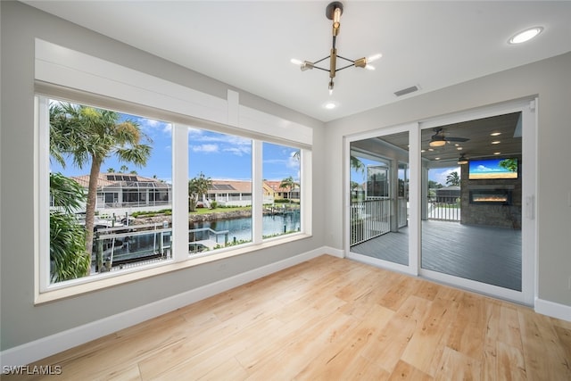 unfurnished room featuring light hardwood / wood-style flooring, a fireplace, a water view, and a notable chandelier