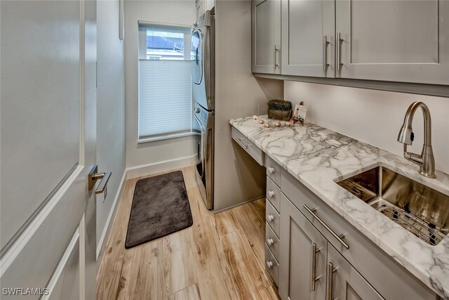 kitchen with stacked washer and clothes dryer, light stone countertops, gray cabinets, light wood-style floors, and a sink