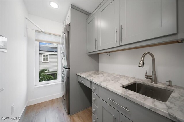 washroom with light hardwood / wood-style flooring, cabinets, stacked washer and dryer, and sink