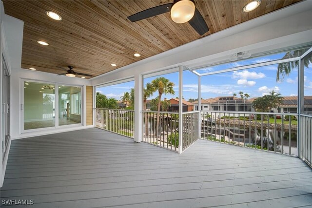 wooden deck featuring a residential view, glass enclosure, a water view, and ceiling fan