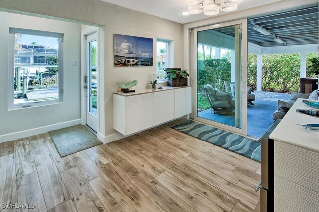 doorway to outside featuring a wealth of natural light, light wood-type flooring, a notable chandelier, and baseboards