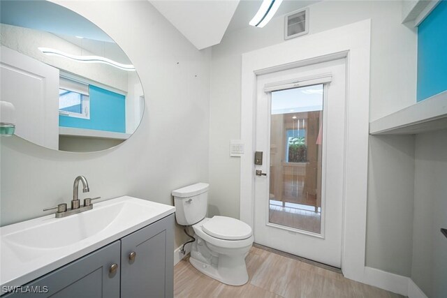 half bathroom with visible vents, vanity, toilet, and baseboards