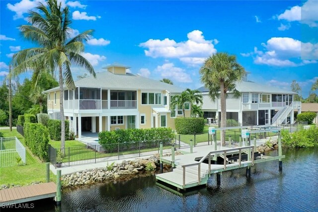 view of dock featuring boat lift, a water view, a lawn, a patio area, and a fenced backyard