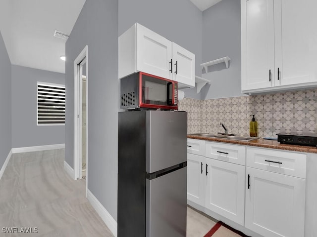 kitchen featuring visible vents, a sink, freestanding refrigerator, and white cabinets