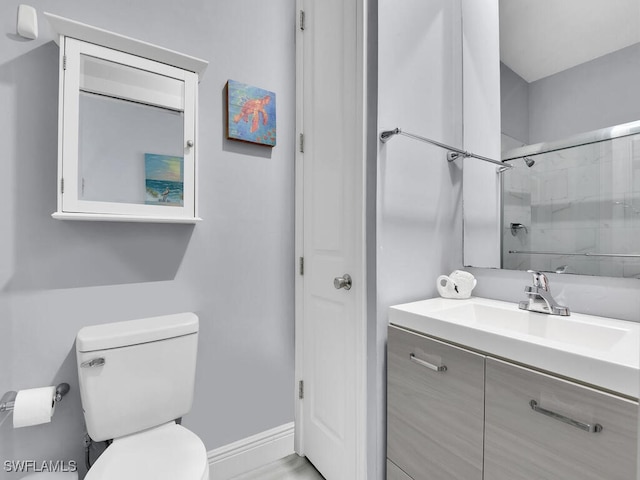 bathroom with toilet, vanity, a shower with shower door, and baseboards