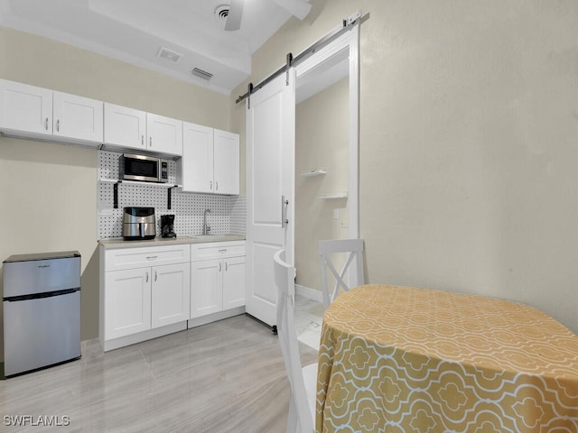 kitchen featuring a barn door, white cabinets, light countertops, appliances with stainless steel finishes, and decorative backsplash