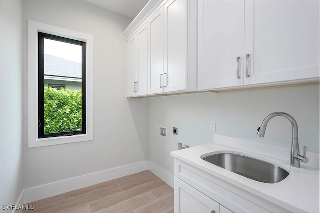 laundry area with light wood finished floors, baseboards, cabinet space, electric dryer hookup, and a sink