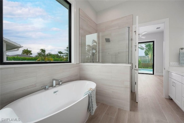 bathroom featuring tile walls, wood finish floors, tiled shower, a soaking tub, and vanity