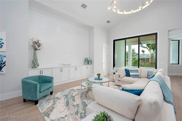 living area with visible vents, baseboards, a chandelier, light wood-type flooring, and high vaulted ceiling