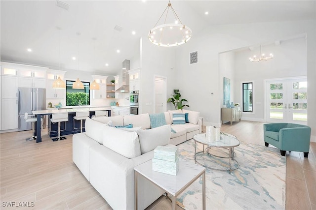 living area featuring a notable chandelier, french doors, light wood-style floors, and visible vents