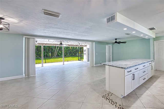 kitchen with ceiling fan, light tile patterned flooring, light stone counters, and white cabinetry